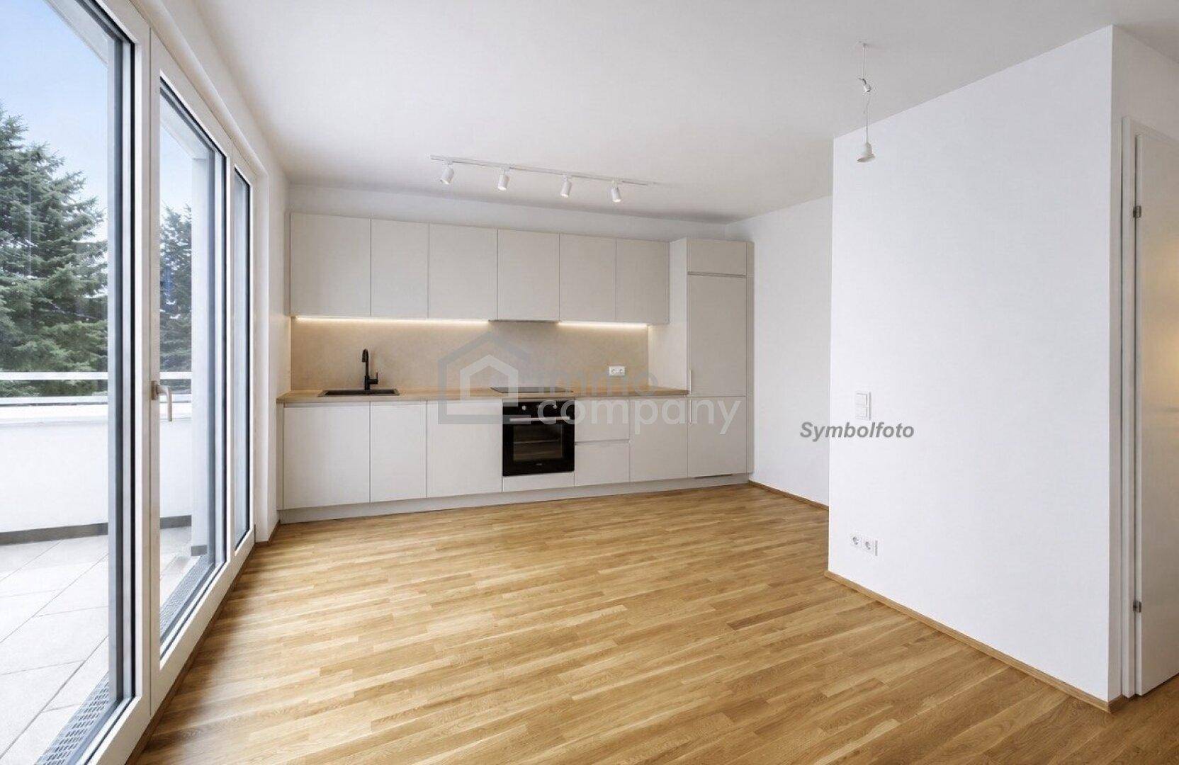 Leere Küche mit modernen weißen Schränken, Holzboden und Zugang zu einem Balkon.