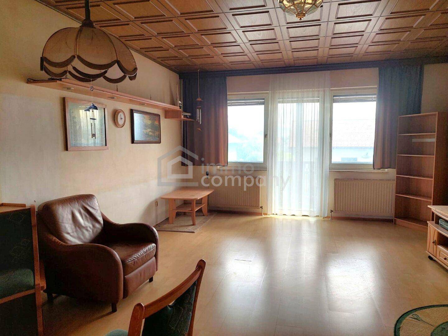 Geräumiges Wohnzimmer mit Ledersessel, Holzboden und dekorativer Deckenverkleidung, gut beleuchtet.