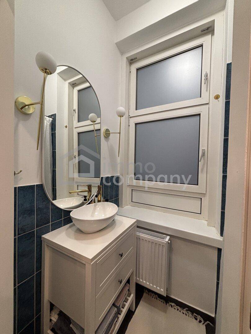 Modernes Badezimmer mit ovalem Spiegel, Waschbecken und Fenster.