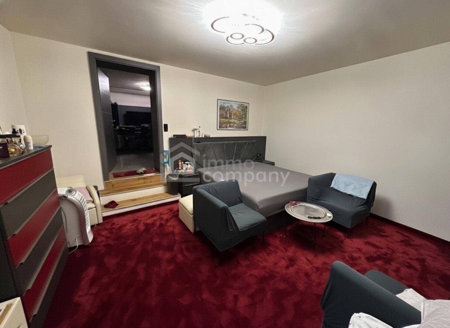 Schlafzimmer mit großem Bett, zwei Sesseln und auffälligem rotem Teppichboden.