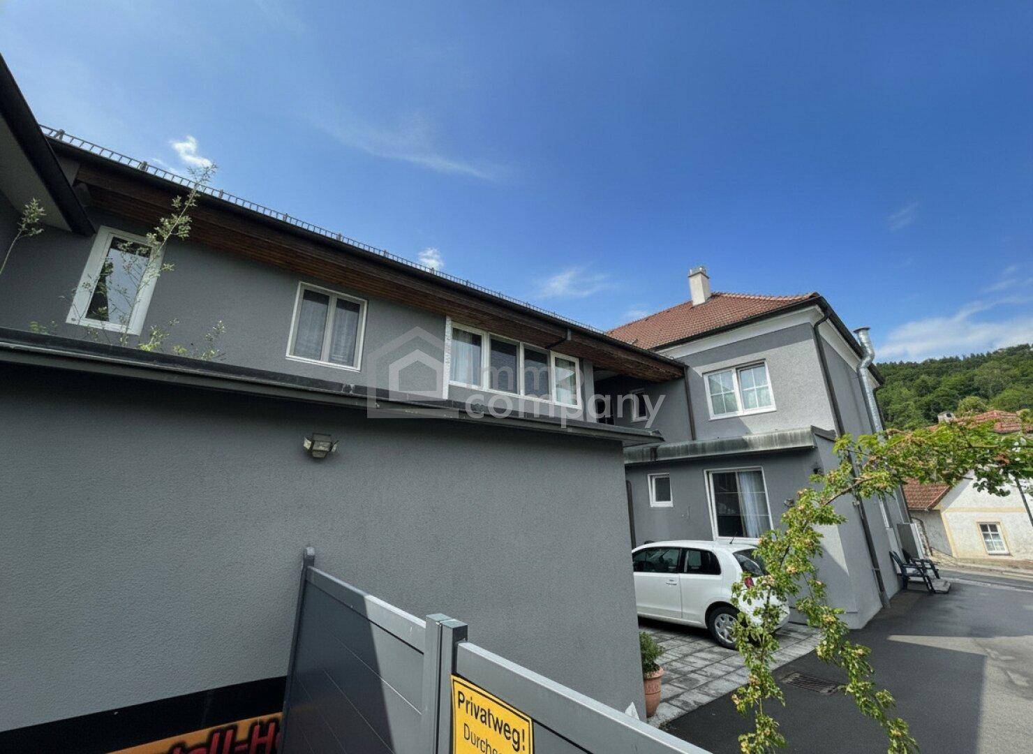 Gut gepflegte Fassade eines Wohnhauses in Grau mit weißen Fenstern und traditionellem Dach.