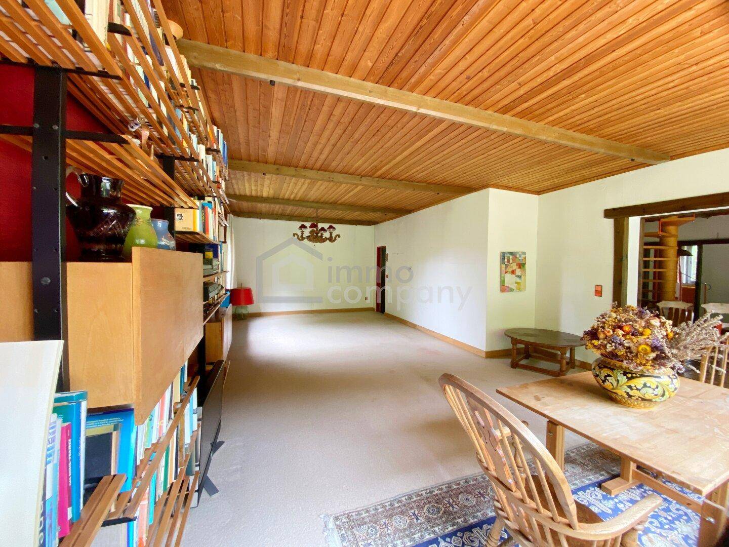 Offener Wohnbereich mit Holzbalkendecke, Bücherregalen und Übergang zu weiteren Räumen.