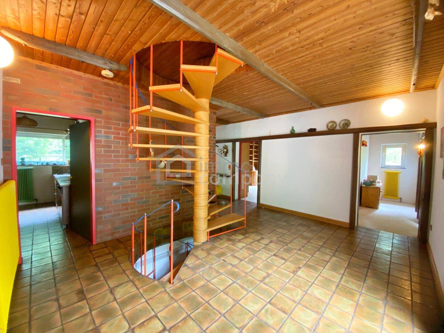 Geräumiger Flur mit Wendeltreppe, gefliestem Boden und sichtbarer Ziegelwand.