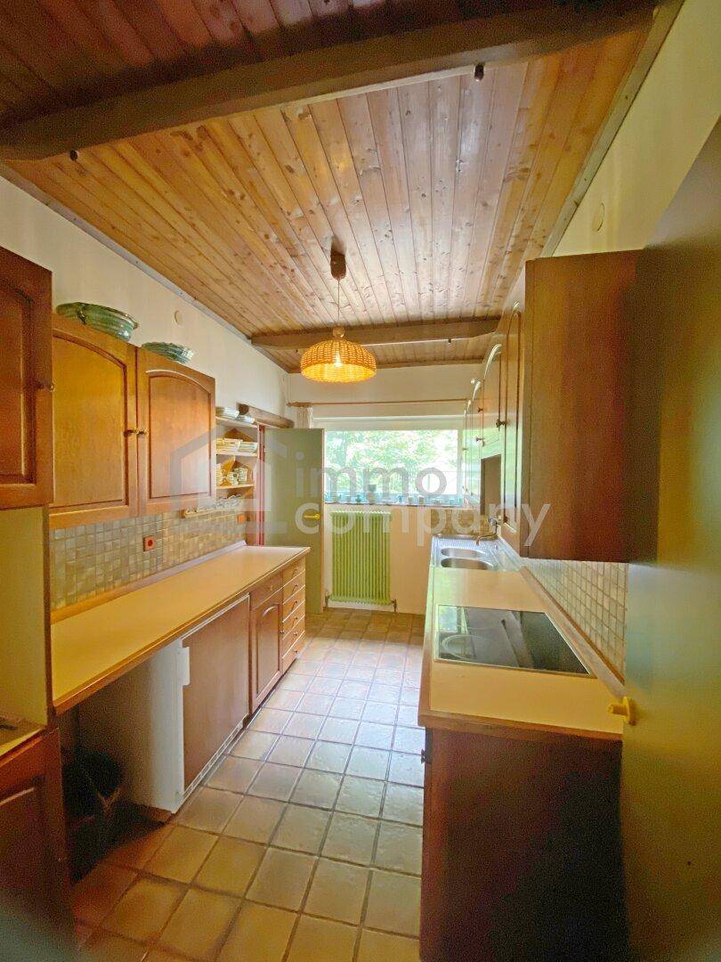 Funktionale Küche mit Holzschränken, gefliestem Boden und Blick ins Grüne durch das Fenster.