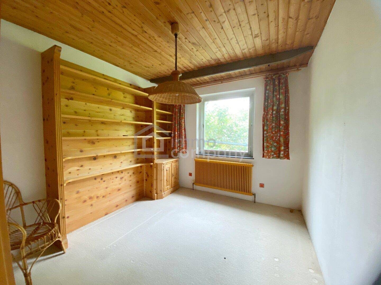 Schlafzimmer oder Arbeitszimmer mit großem Einbauregal aus Holz und Fenster.