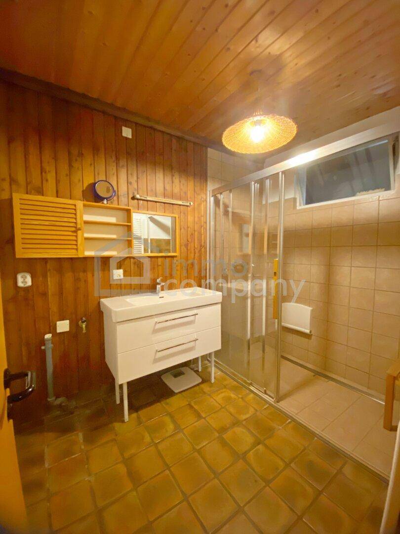 Badezimmer mit Holzverkleidung, gefliestem Boden, Einzelwaschbecken und Duschkabine.