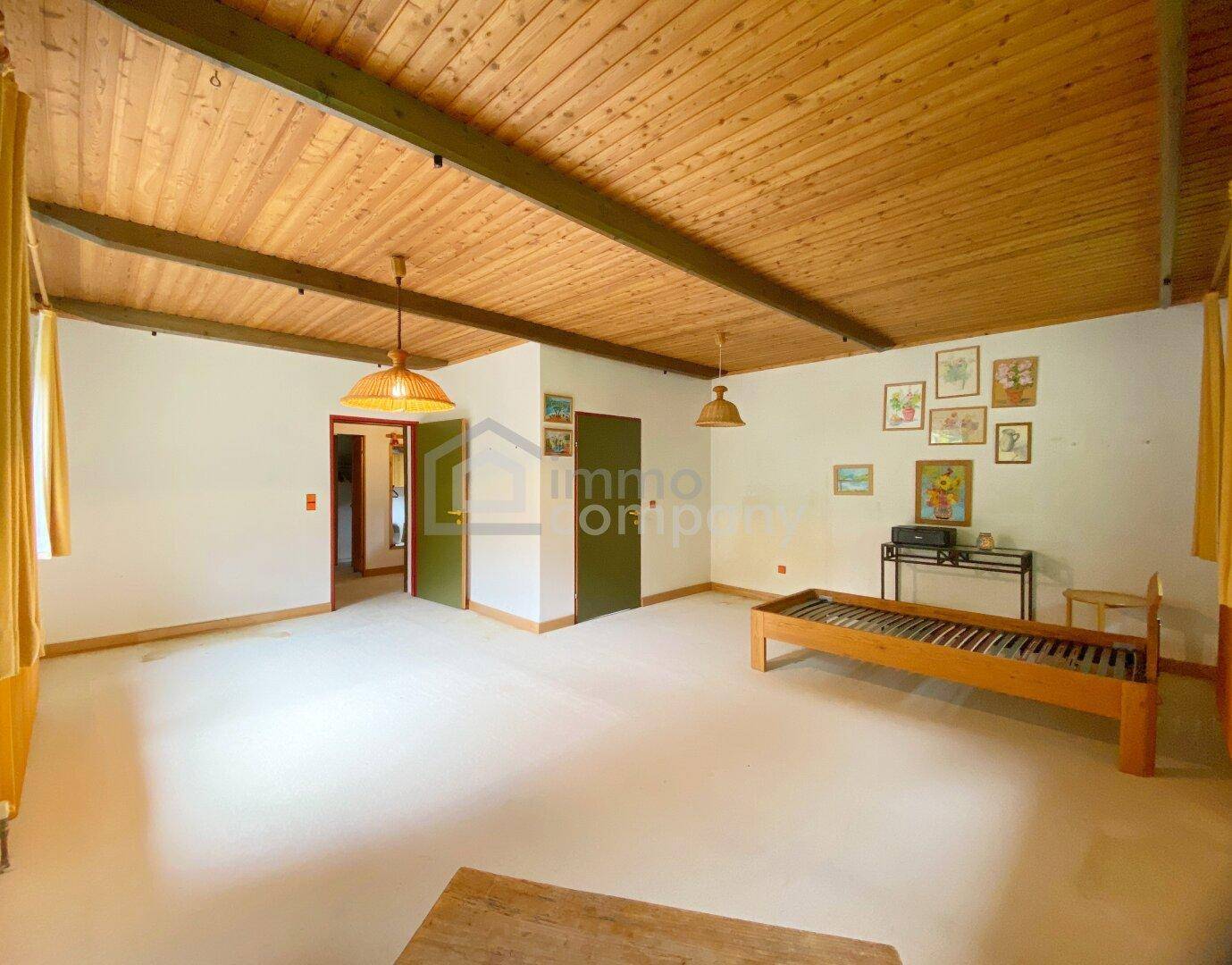 Helles Schlafzimmer mit Holzbalkendecke, Teppichboden und einfacher Einrichtung.