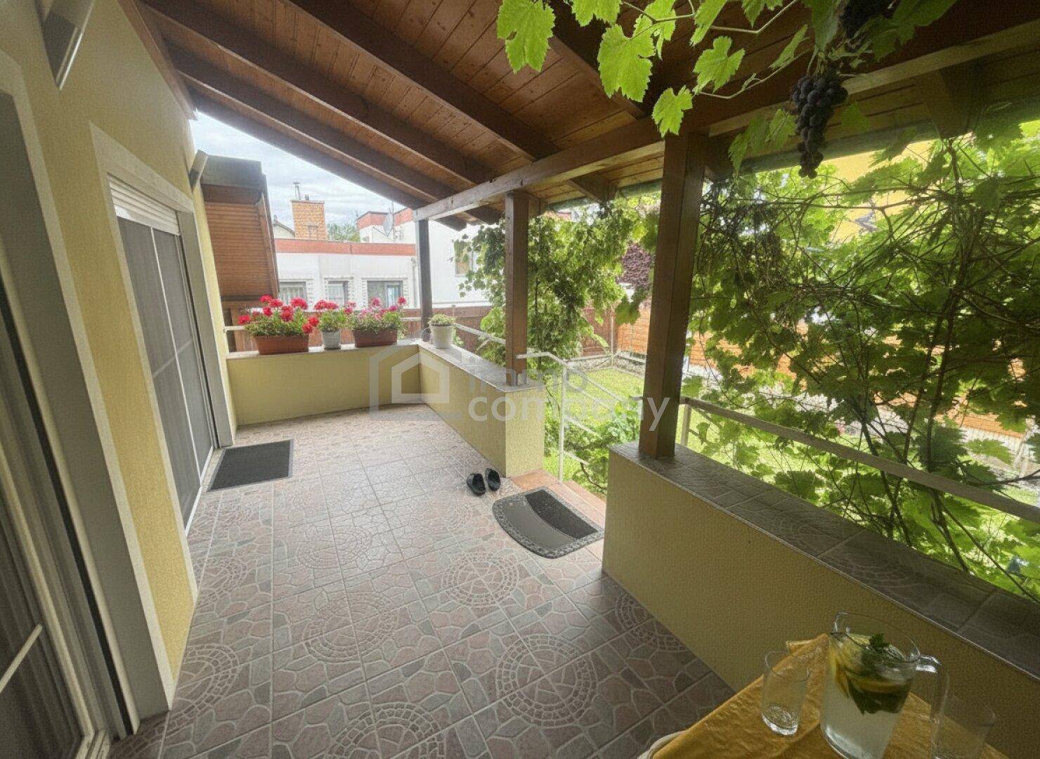 Überdachter Balkon mit Fliesenboden, Holzbalkendecke und üppigen Weinreben.
