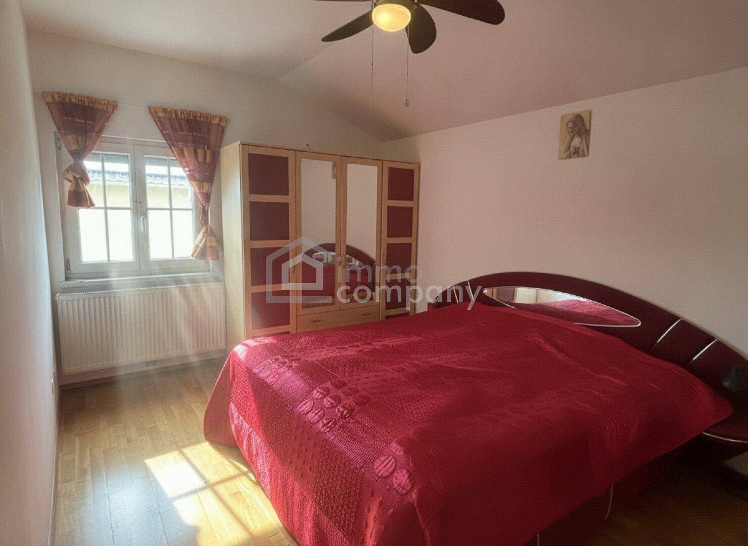 Schlafzimmer mit rotem Bett und Kleiderschrank, Holzboden und Dachschräge.