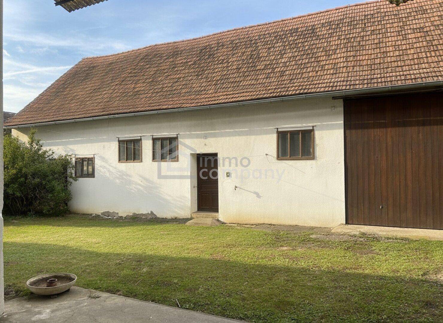 Ländliches Nebengebäude mit großem Scheunentor und traditionellem Ziegeldach, umgeben von einer Wiese.