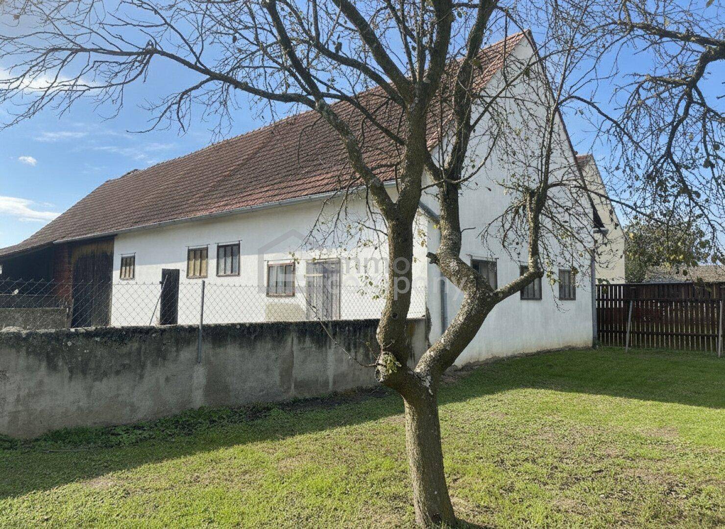 Weißes Landhaus mit traditionellem Ziegeldach, umgeben von einer grünen Wiese und einem alten Baum.