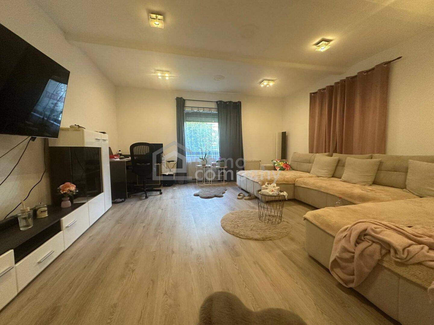 Geräumiges Wohnzimmer mit großem Ecksofa, Schreibtischbereich und Laminatboden, gut beleuchtet.