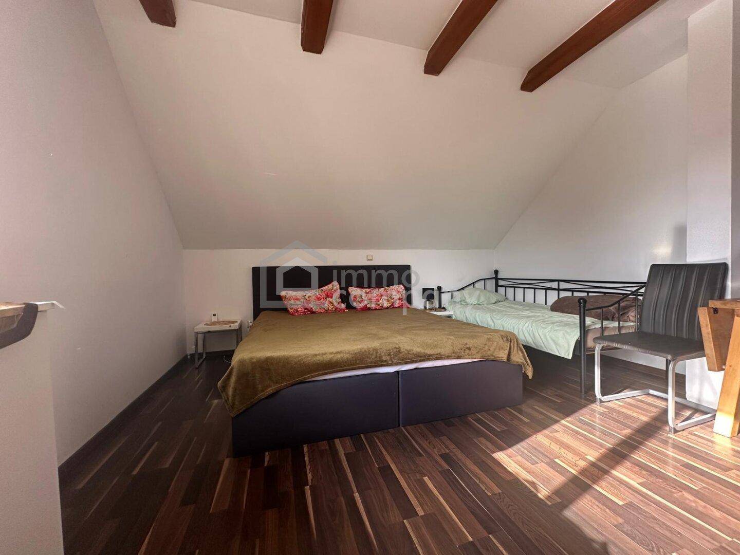 Gemütliches Schlafzimmer im Dachgeschoss mit Holzbalken, zwei Betten und dunklem Holzboden.
