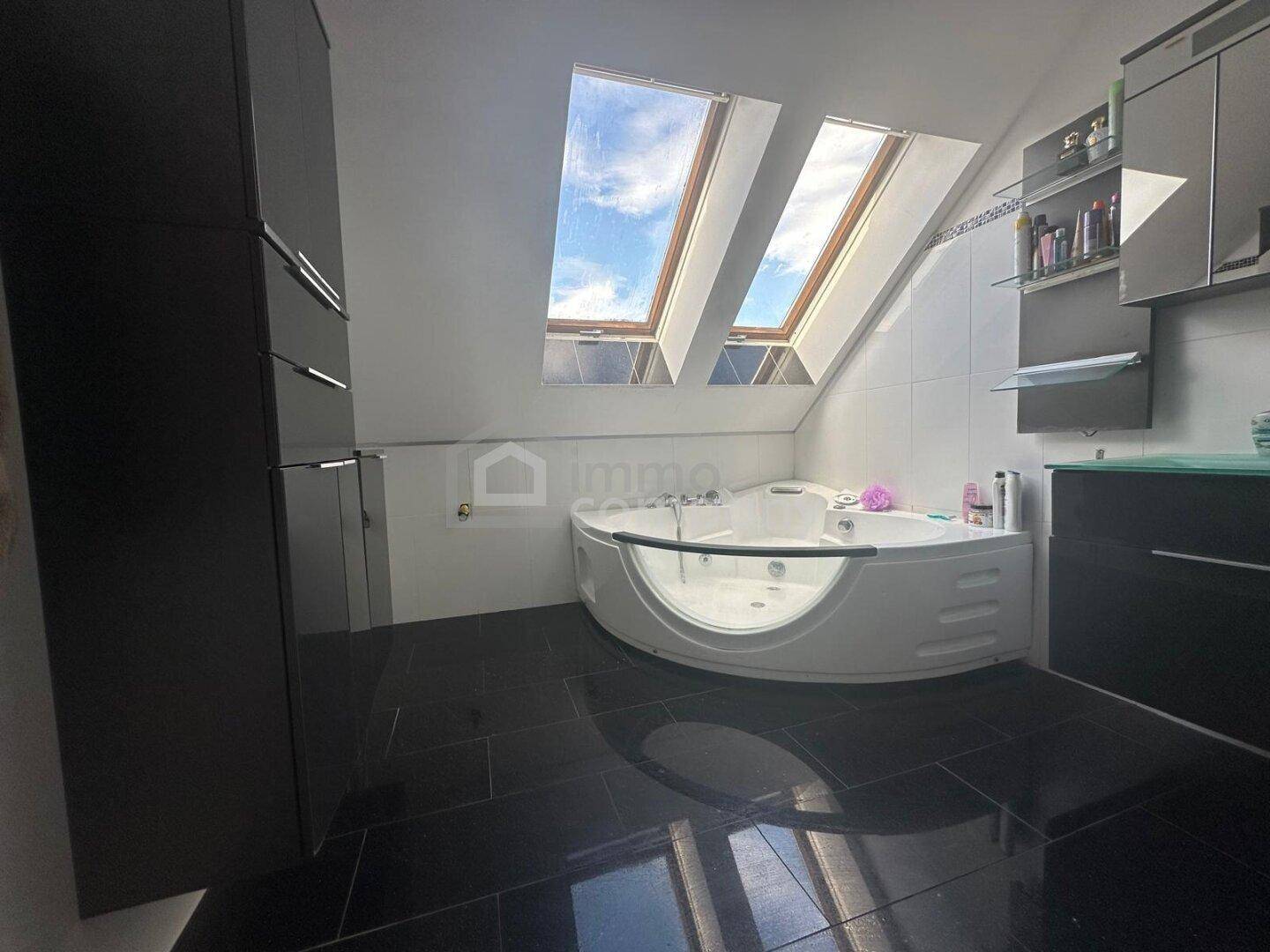 Modernes Badezimmer im Dachgeschoss mit Eckbadewanne, Dachfenstern und dunklen Fliesen.