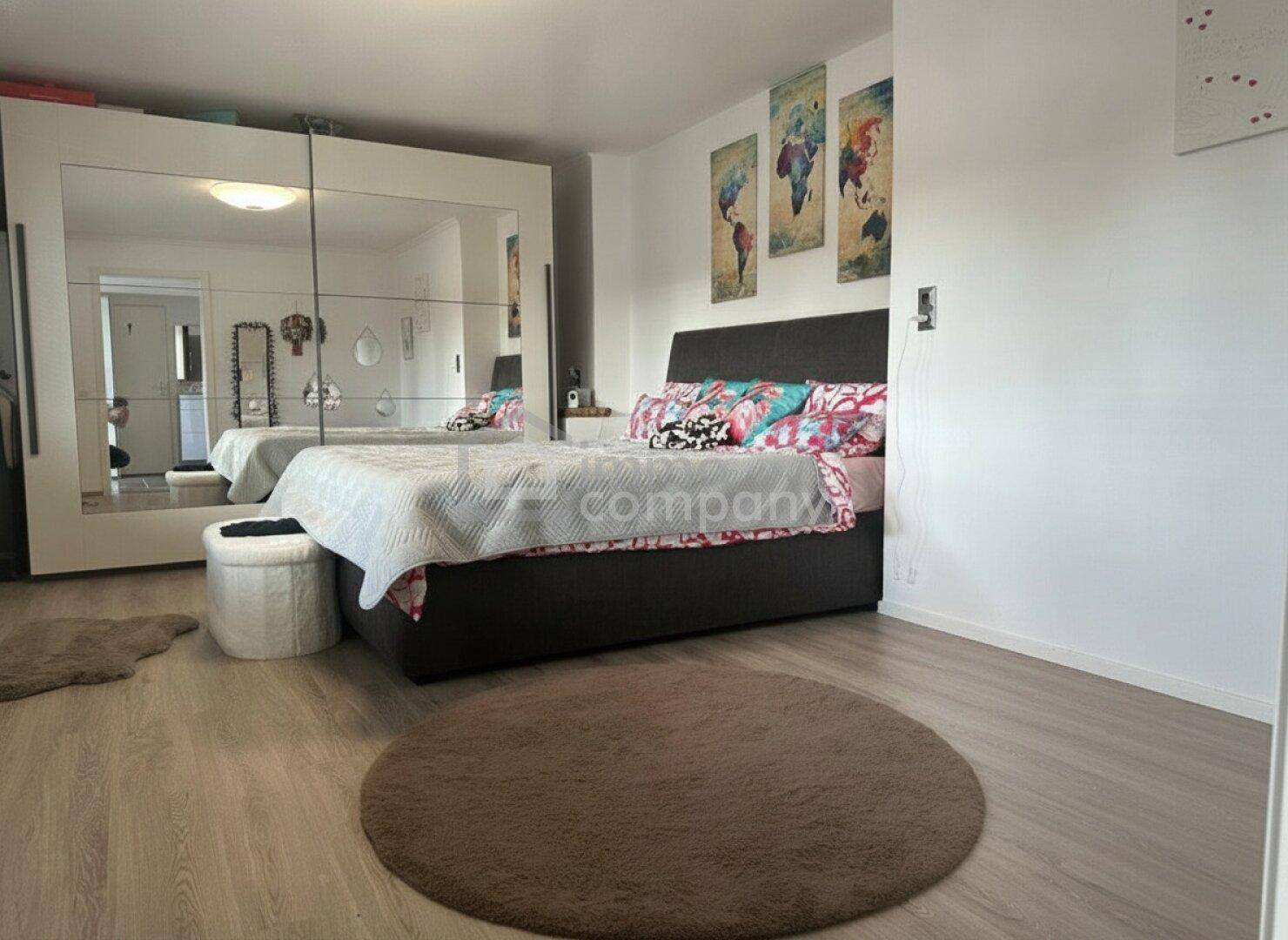 Helles Schlafzimmer mit großem Bett, Spiegelschrank und Holzboden, dekoriert mit Weltkartenbildern.