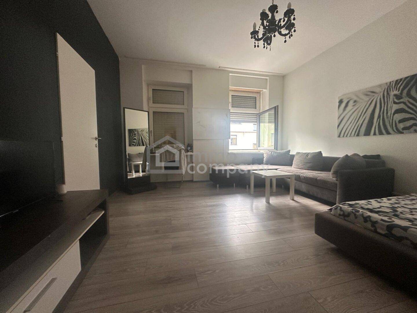 Helles Wohnzimmer mit Laminatboden, dunkler Akzentwand und Kronleuchter, bietet viel Tageslicht.