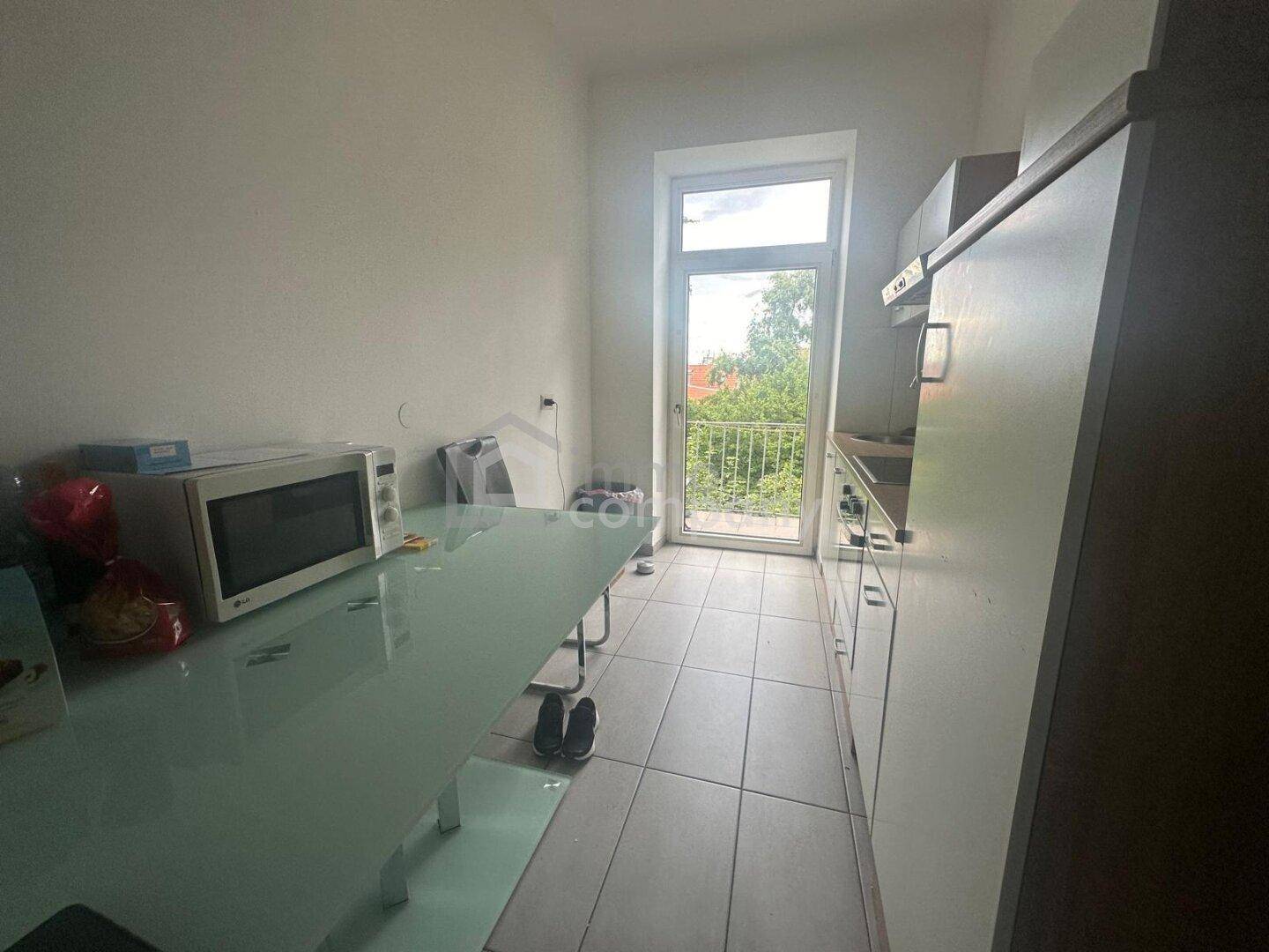 Schmale Küche mit Fliesenboden, weißer Einrichtung und direktem Zugang zum Balkon.
