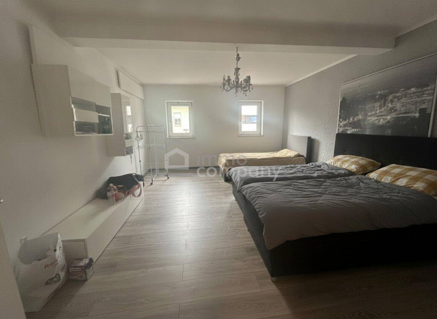 Geräumiges Schlafzimmer mit zwei Betten, Laminatboden und einem eleganten Kronleuchter.