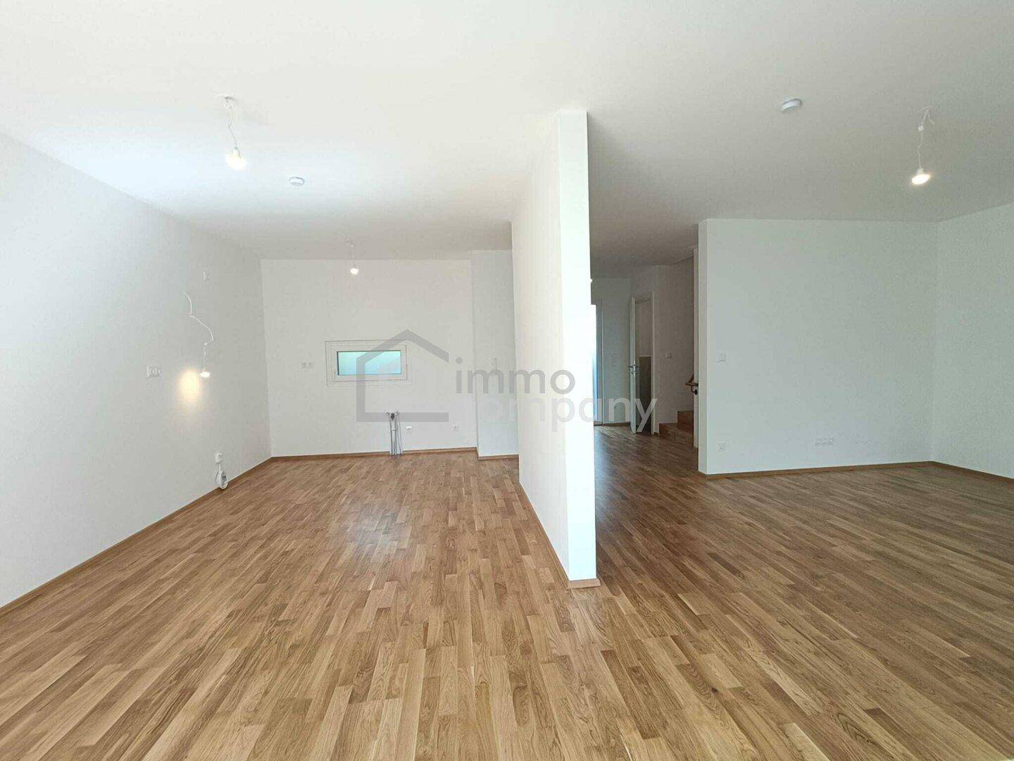 Geräumiger, heller Innenraum mit Holzboden und weiß gestrichenen Wänden, ideal für offenes Wohnen.