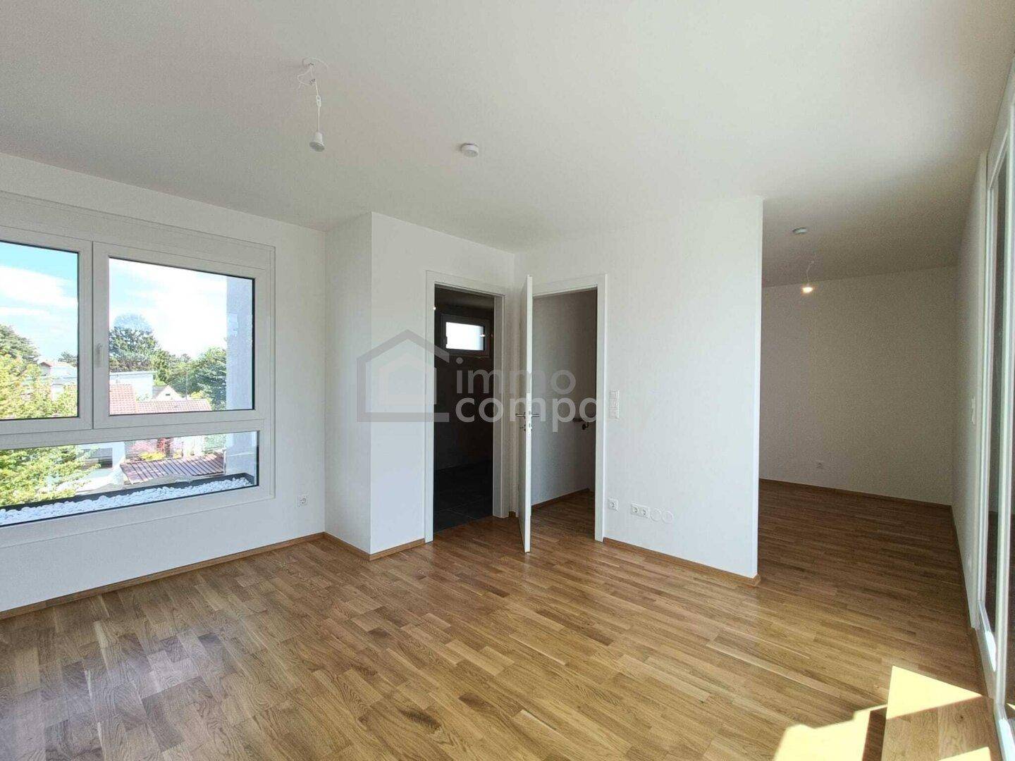 Helles Zimmer mit Holzboden und großem Fenster, das einen Blick ins Grüne bietet.