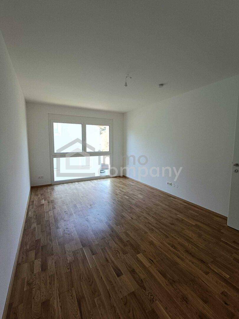 Leeres Schlafzimmer mit Holzboden und Zugang zu einem potenziellen Außenbereich durch die Fenstertür.