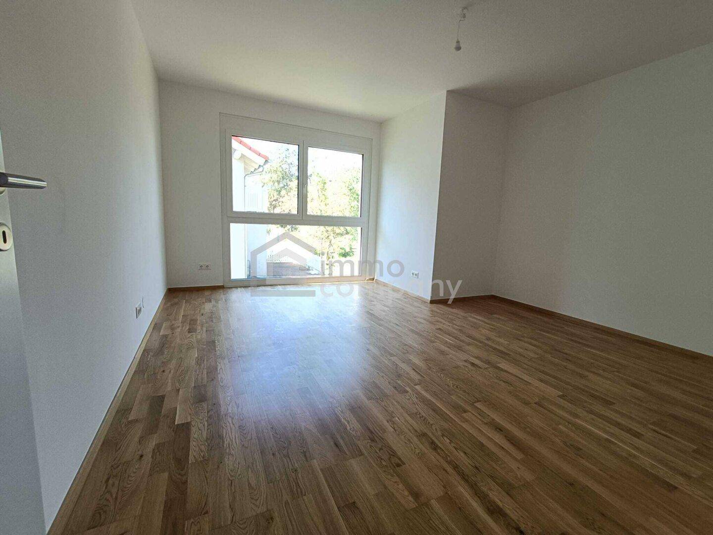 Freundliches Zimmer mit Holzboden und großem Fenster, das viel Tageslicht hereinlässt.