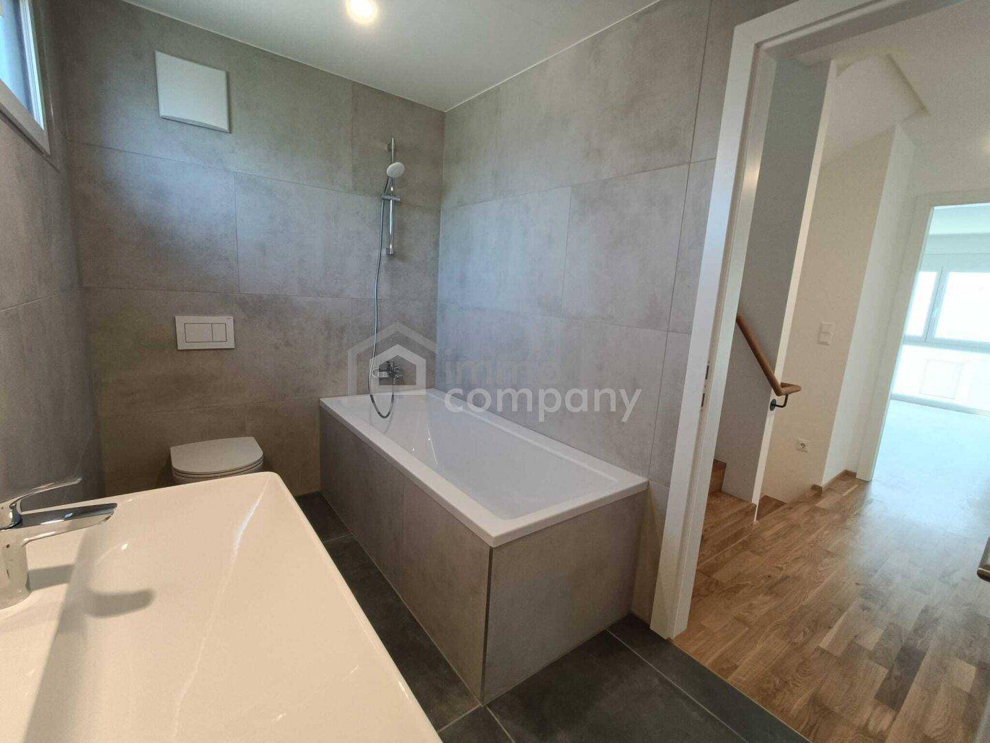 Modernes Badezimmer mit grauen Fliesen, Badewanne, WC und Einzelwaschbecken.