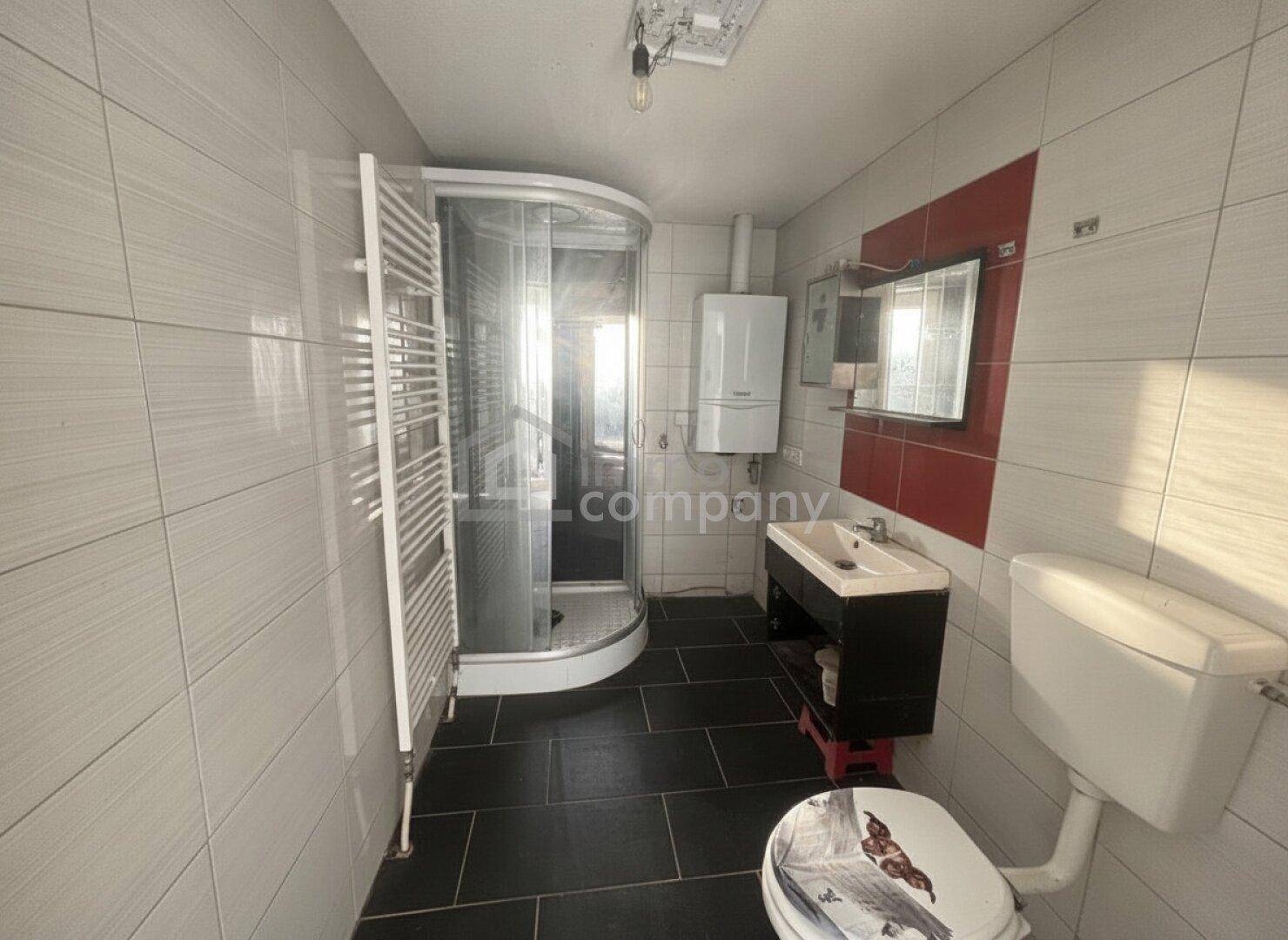 Modernes Badezimmer mit Duschkabine, WC, Waschbecken und beheiztem Handtuchhalter.