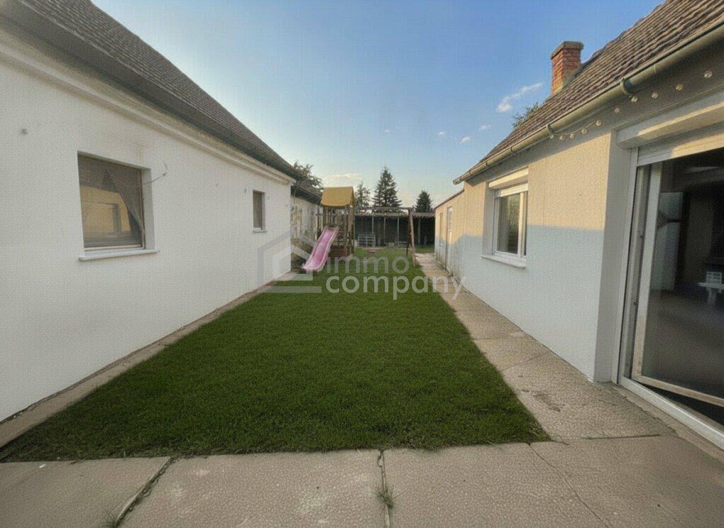 Grüner Gartenbereich zwischen zwei Gebäuden mit einem Spielplatz im Hintergrund.