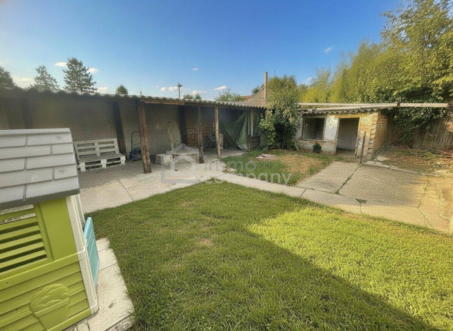 Hinterhof mit Rasenfläche, befestigten Wegen und einem überdachten Sitzbereich im Freien.