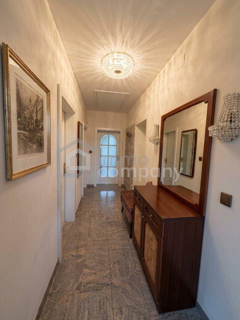 Heller Flur mit eleganten Fliesen, einem Spiegel und einem funkelnden Deckenleuchter.