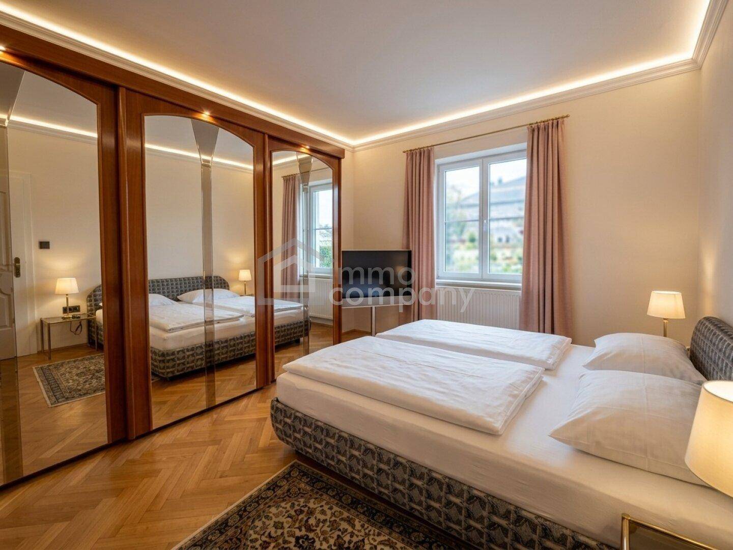 Schlafzimmer mit Doppelbett, großen Spiegelschränken und klassischem Parkettboden.