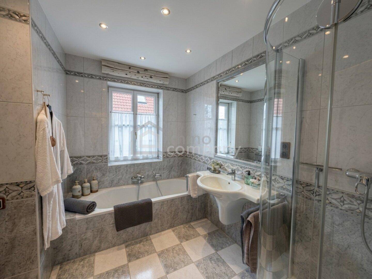 Badezimmer mit Badewanne, Dusche, Waschbecken und hellgrauen Fliesen sowie einem Fenster.