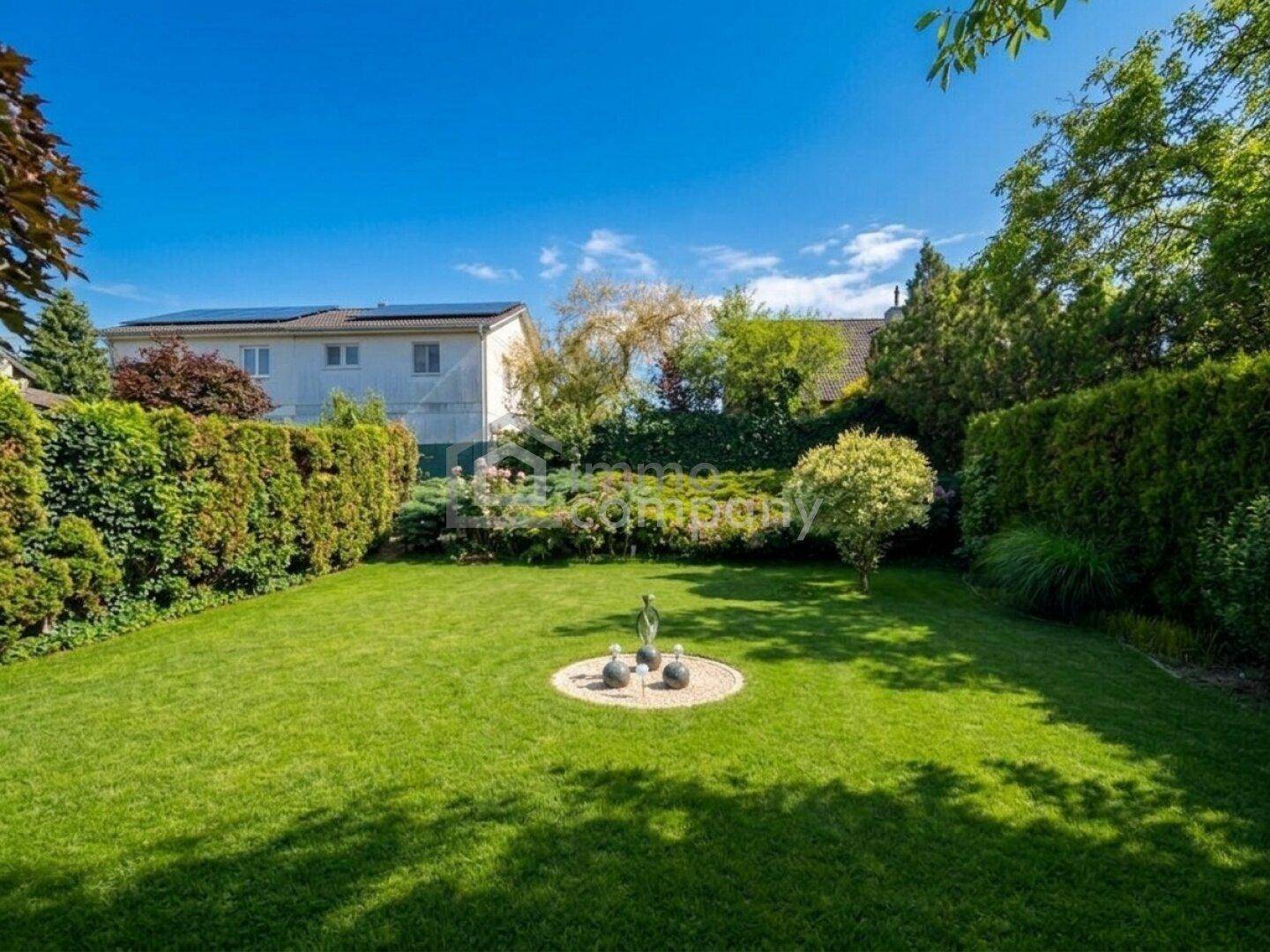 Weitläufiger Garten mit gepflegtem Rasen, hohen Hecken und einem Haus mit Solaranlage im Hintergrund.