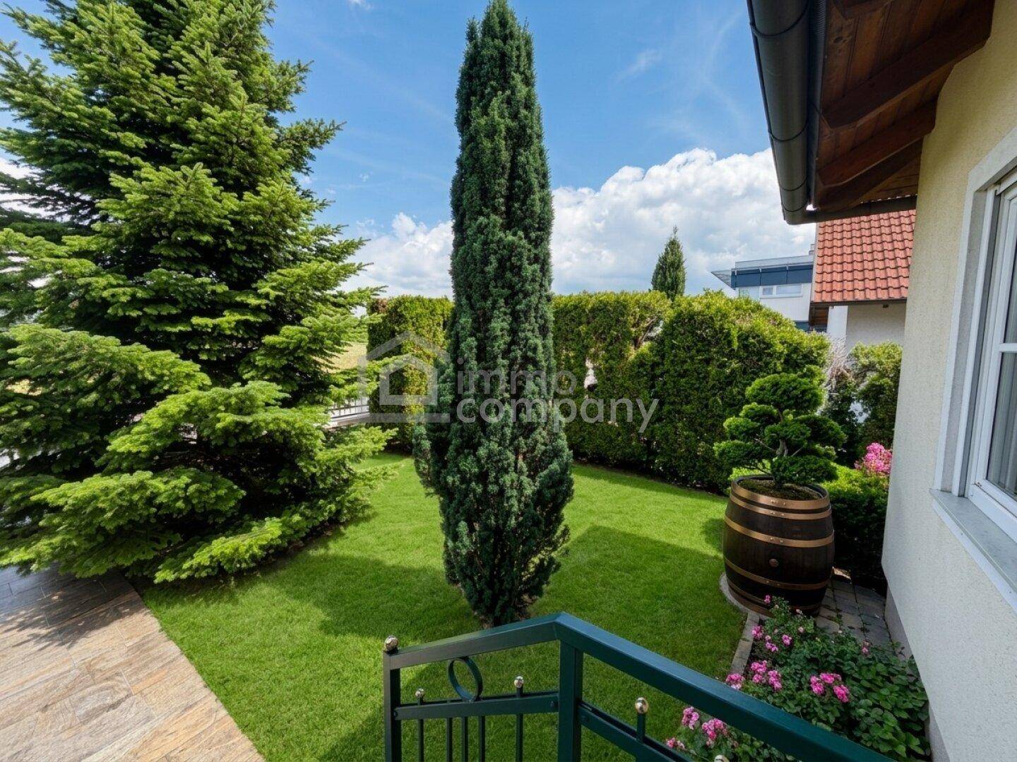 Seitlicher Blick auf das Haus mit gepflegtem Rasen, hohen Bäumen und einem Gartenweg.