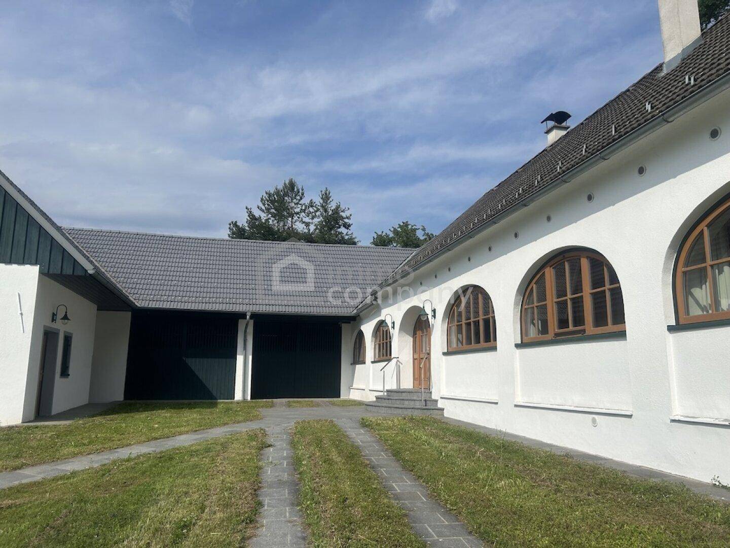Seitenansicht des Hauses mit gepflasterter Auffahrt, Garagentoren und Rundbogenfenstern.