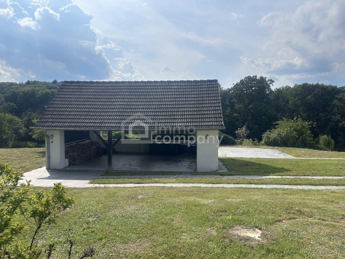 Offener Carport oder Unterstand in einer weitläufigen Grünfläche mit Blick in die Natur.