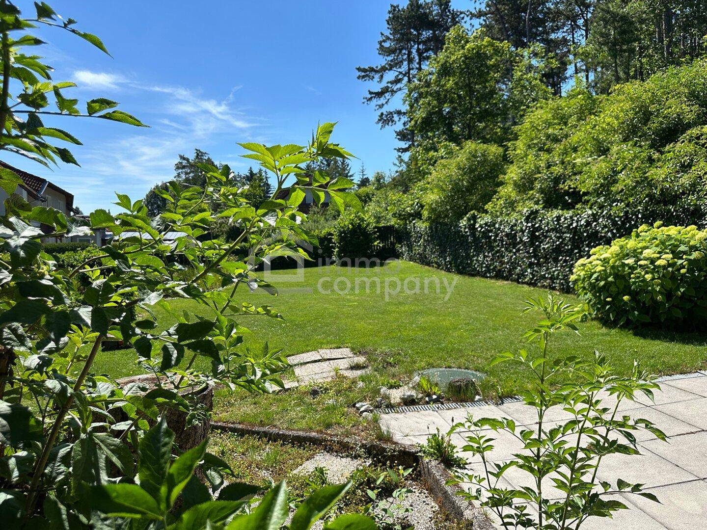 Gepflegte Rasenfläche im Garten mit Steinplatten und üppiger Bepflanzung im Hintergrund.