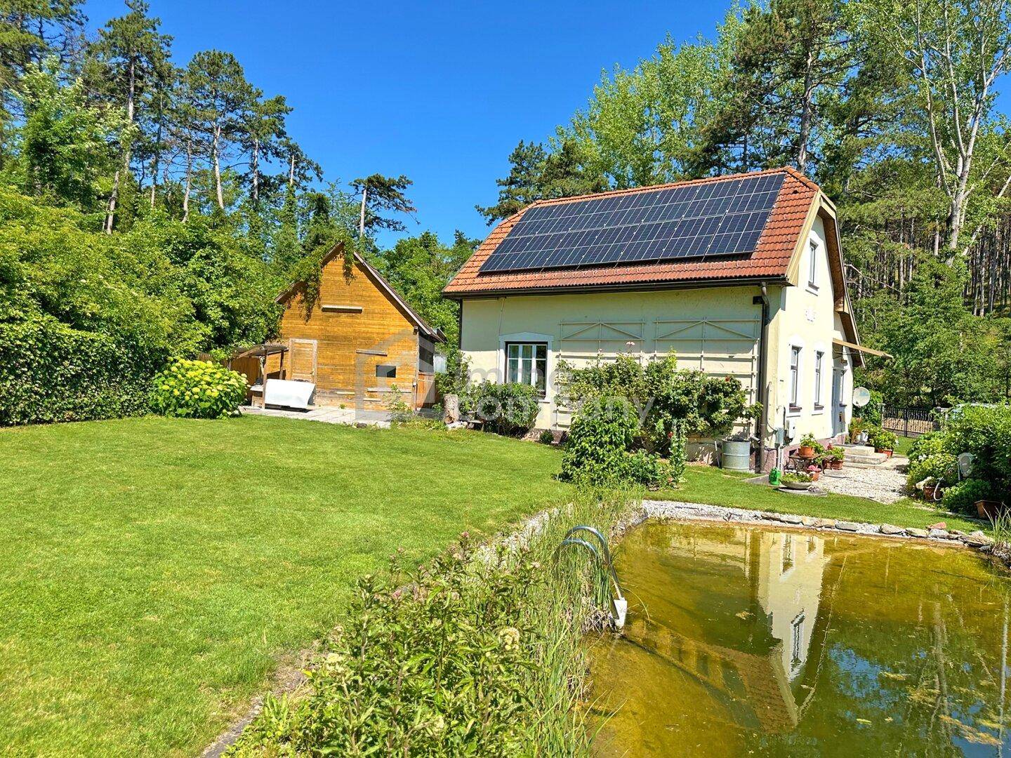 Haus mit Photovoltaikanlage und großem Garten, inklusive Teich und weitläufiger Rasenfläche.