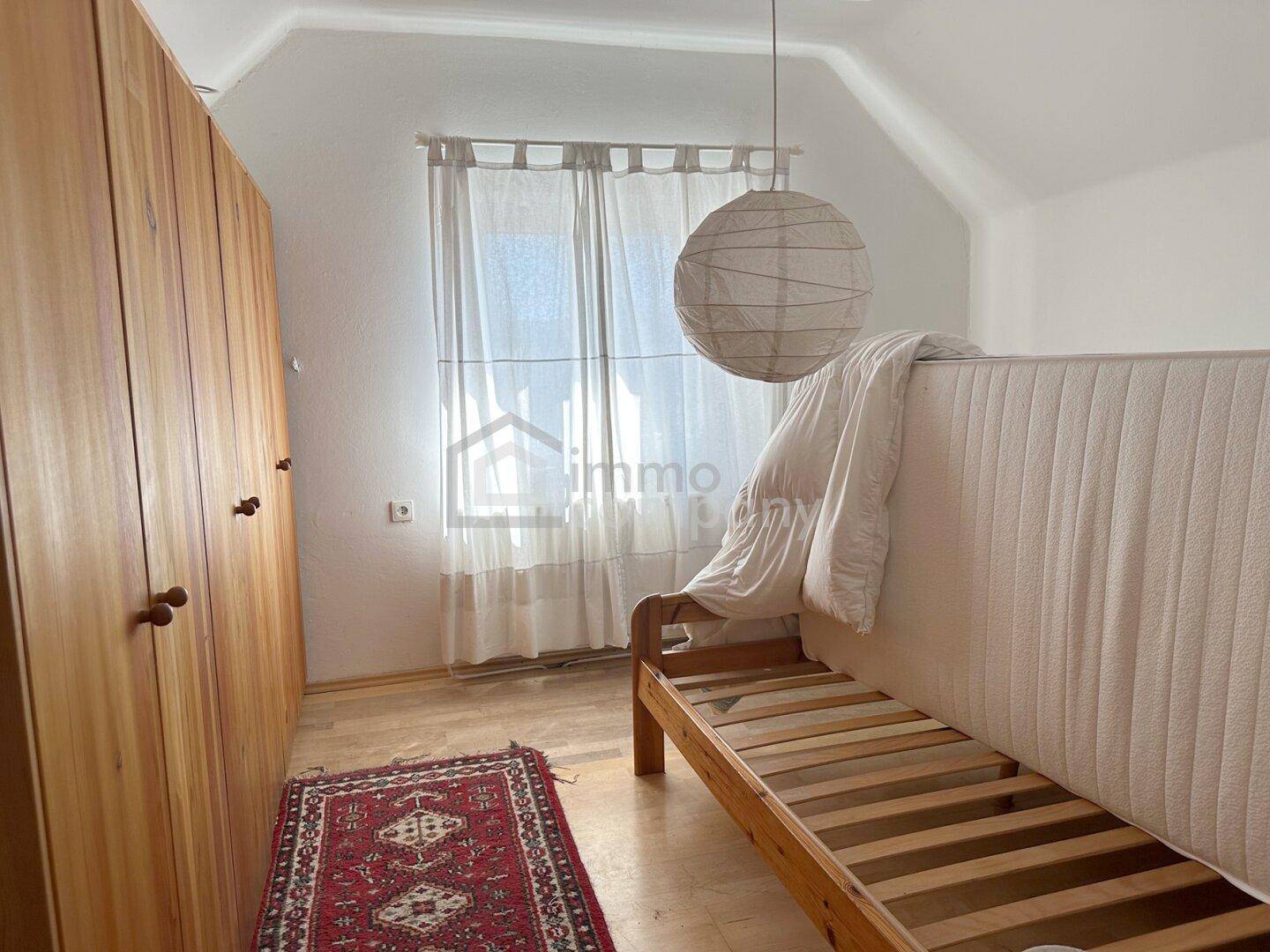 Schlafzimmer im Dachgeschoss mit Holzboden, Kleiderschrank und einem Bettgestell unter der Dachschräge.