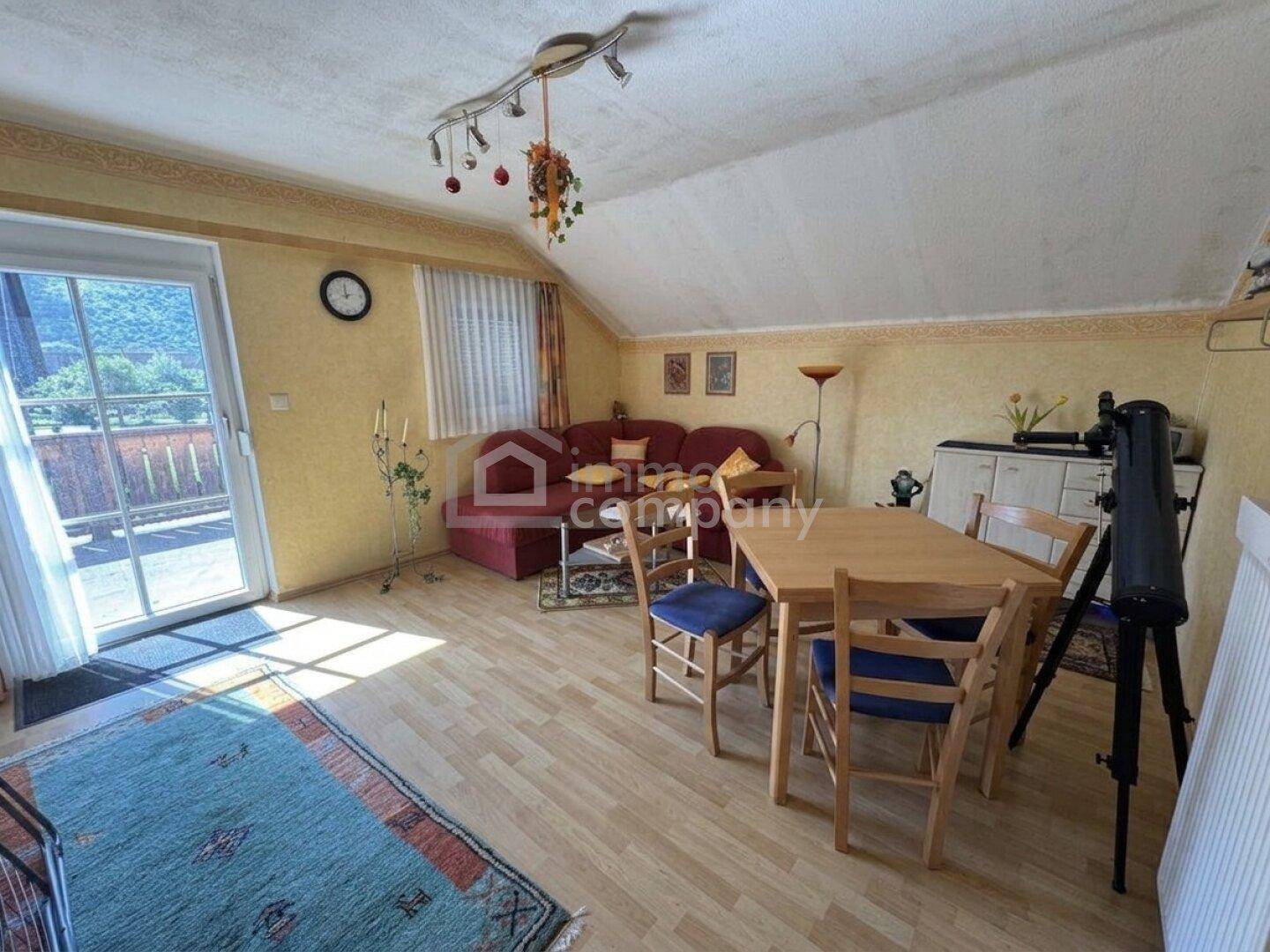 Gemütlicher Wohn-Essbereich mit Laminatboden, Dachschräge und Zugang zu einem Balkon.