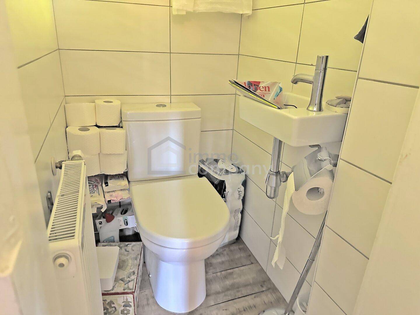 Kleines Gäste-WC mit Toilette, kleinem Waschbecken und Heizkörper, einfach und funktional.
