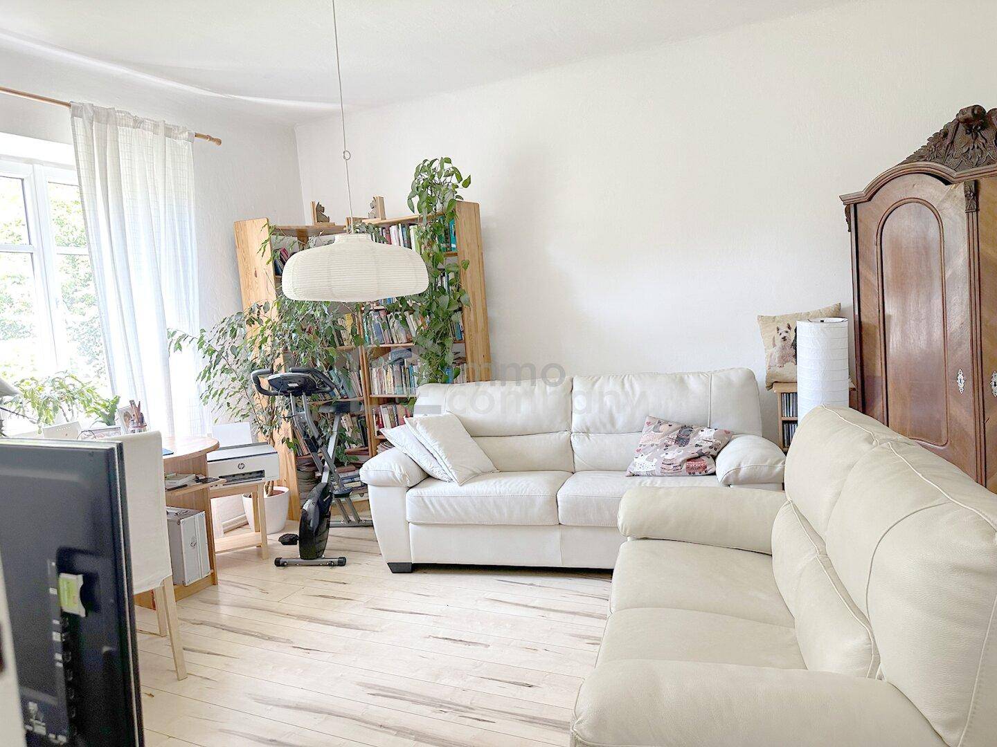Wohnzimmer mit weißer Ledercouch, Holzboden und Bücherregalen, bietet eine helle und wohnliche Atmosphäre.