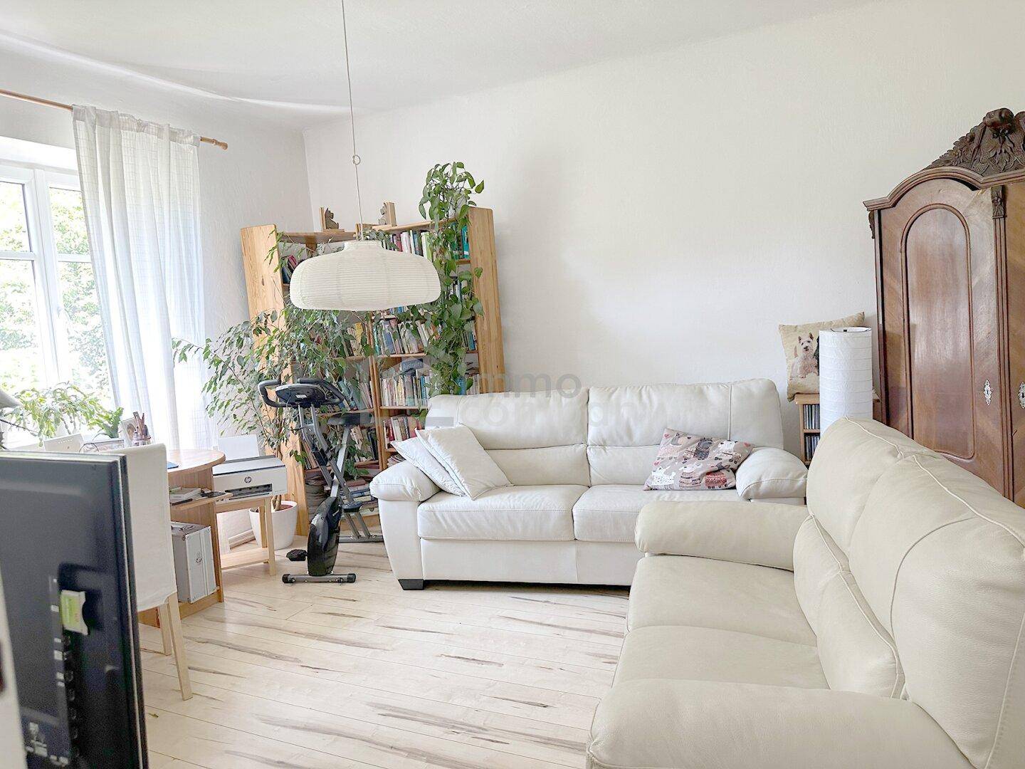 Wohnzimmer mit weißer Ledercouch, Holzboden und Bücherregalen, bietet eine helle und wohnliche Atmosphäre.