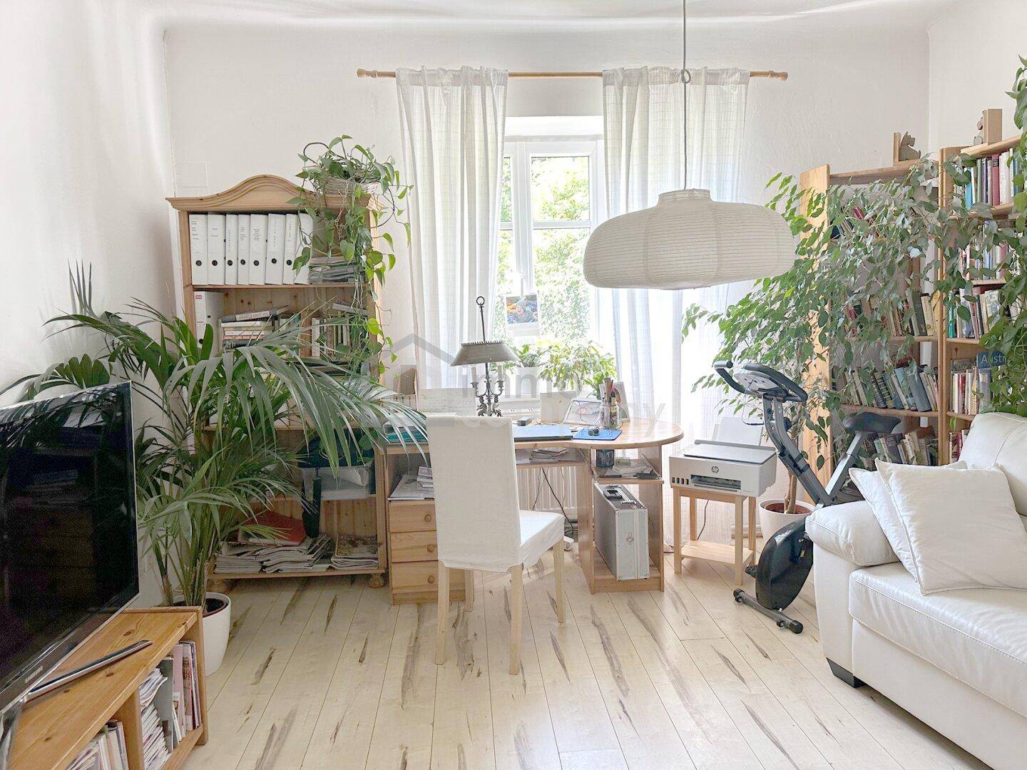 Heller Wohnbereich mit Schreibtisch, weißem Sofa und vielen Pflanzen, ideal für Arbeit und Entspannung.