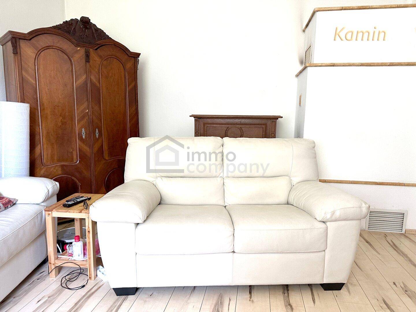 Wohnzimmer mit weißem Sofa und antikem Holzschrank, daneben ein Kamin, der Wärme verspricht.