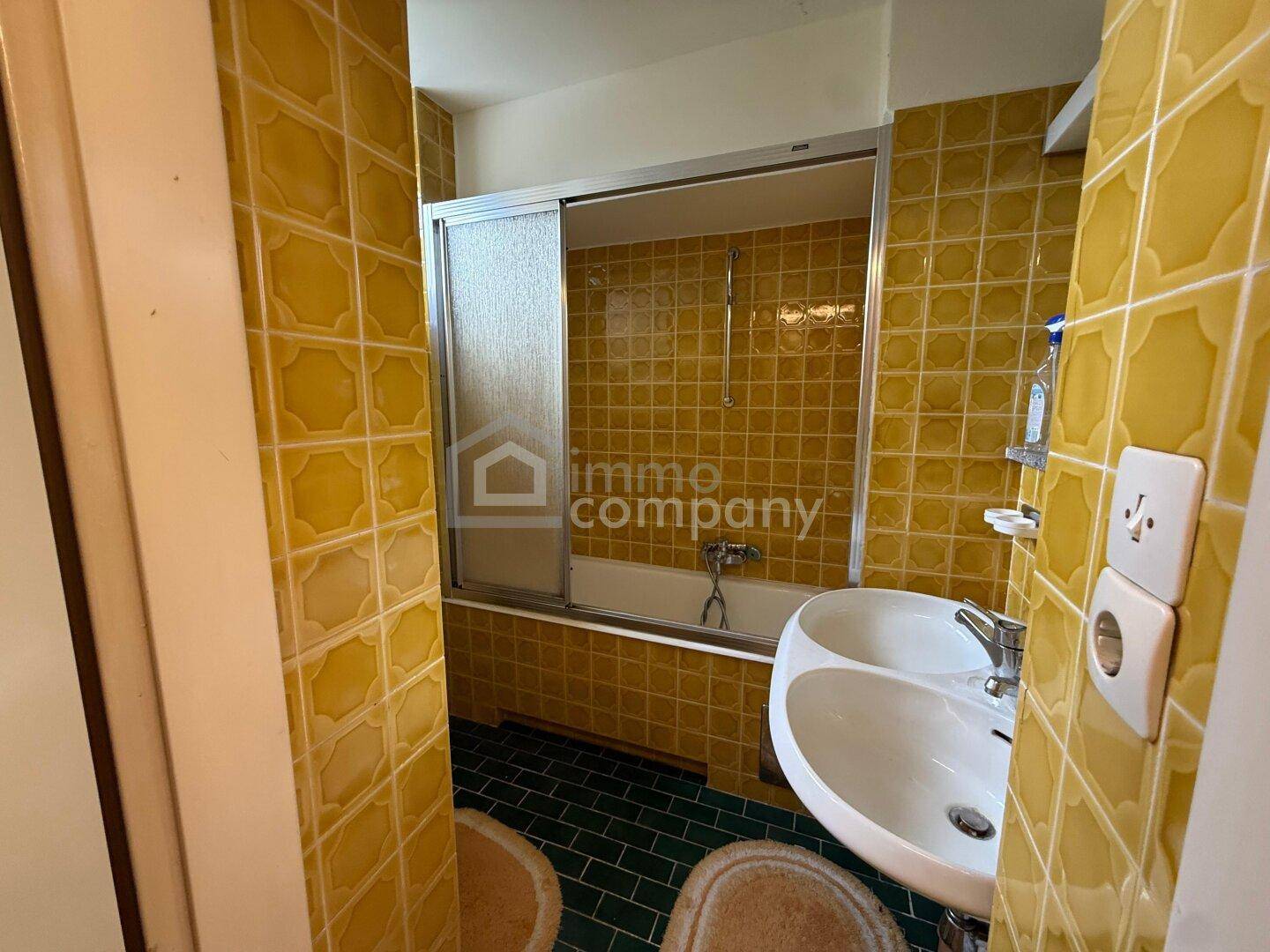 Badezimmer mit gelben Fliesen, Badewanne mit Duschwand und Waschbecken.