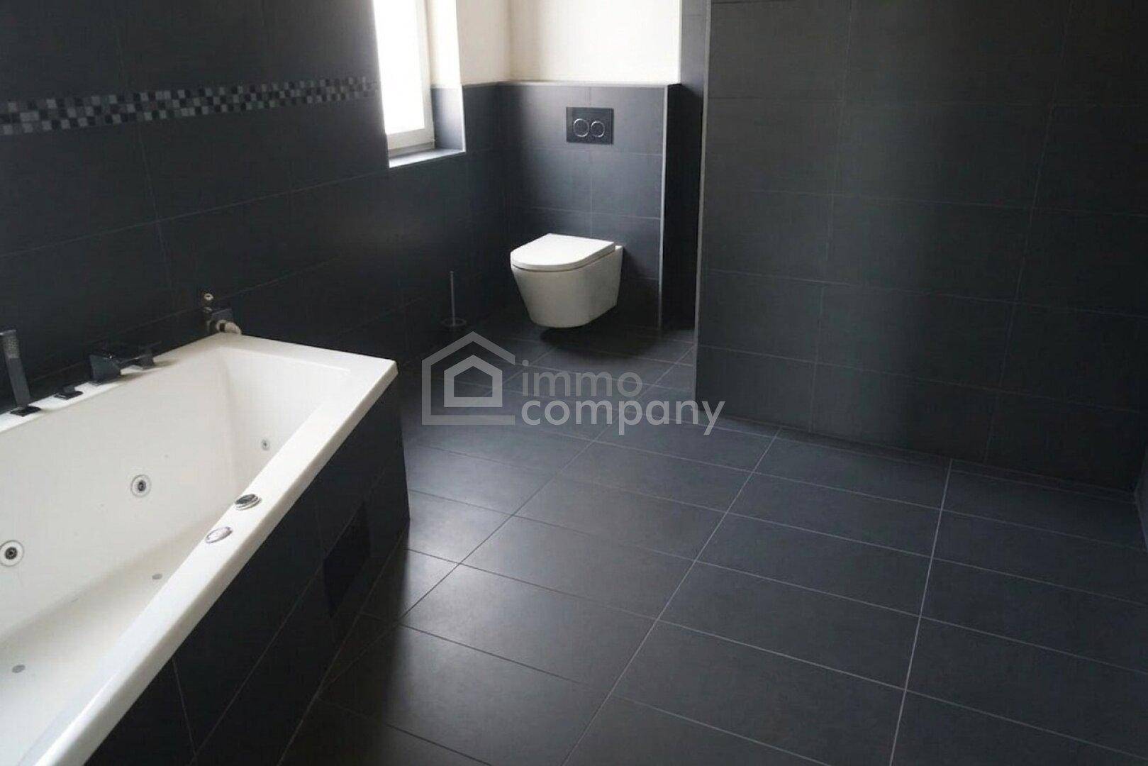 Modernes Badezimmer mit dunklen Fliesen, Whirlpool-Badewanne und Wand-WC.