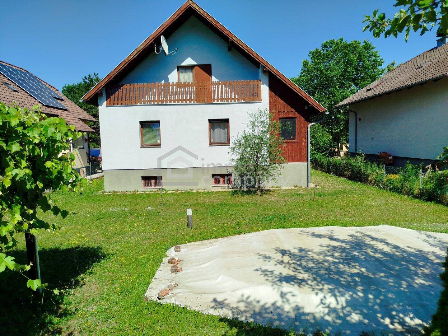 Hausfassade mit Balkon und großem Gartenbereich, teilweise mit Abdeckung auf dem Rasen.