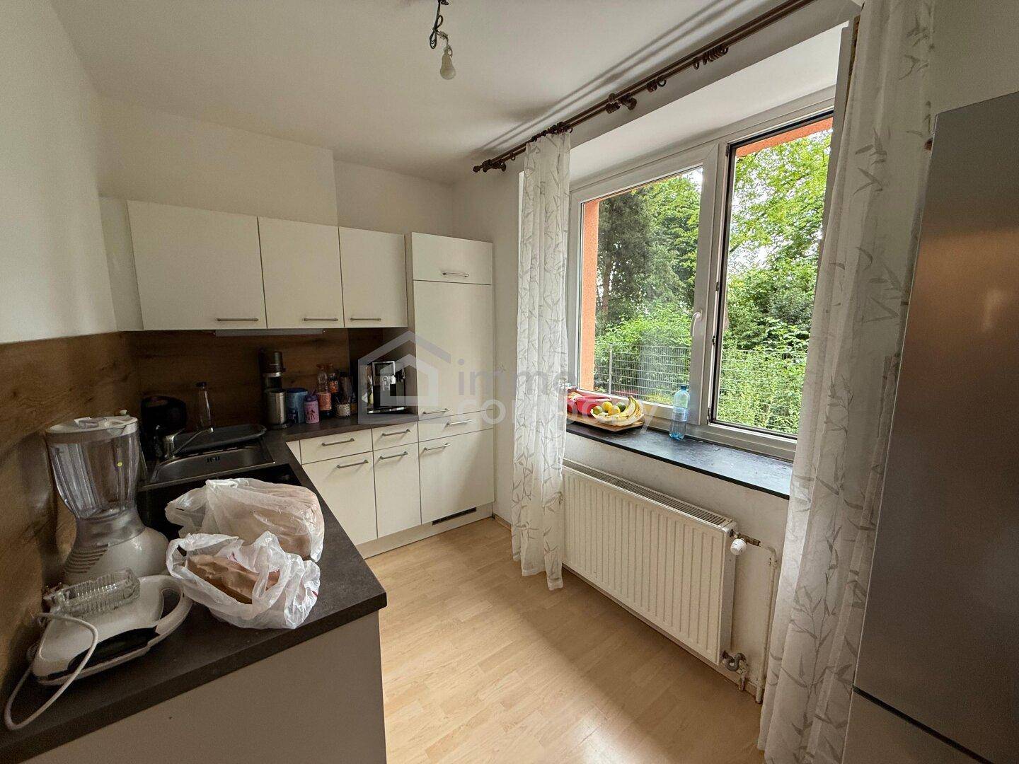 Helle Küche mit weißen Schränken, dunkler Arbeitsplatte und großem Fenster mit Grünblick.